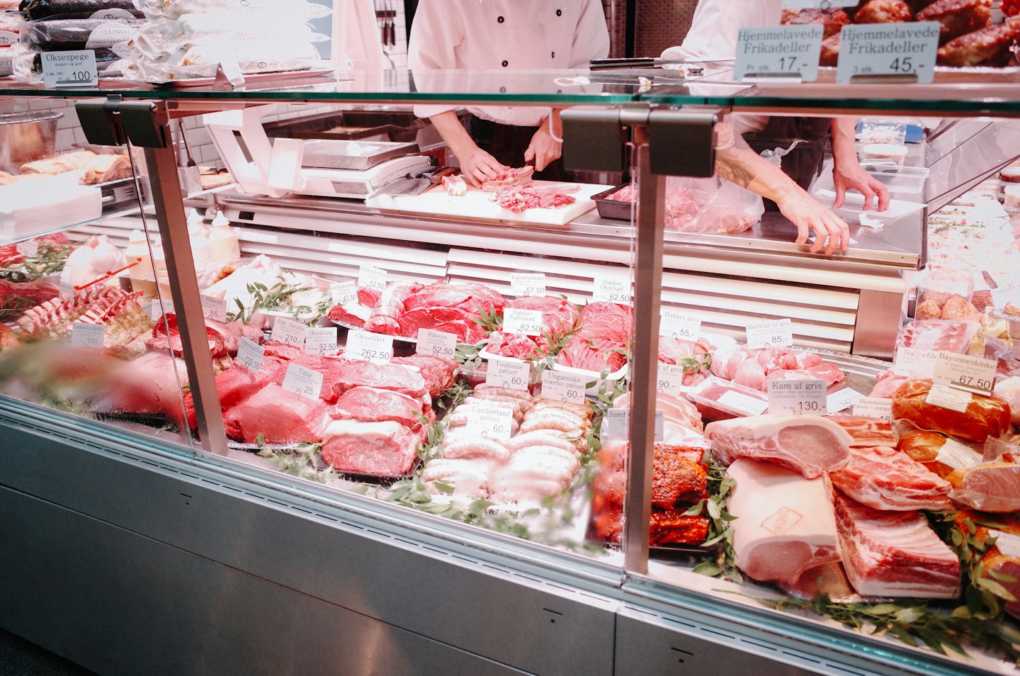 Butchers prepare fresh cuts of meat at a deli counter.