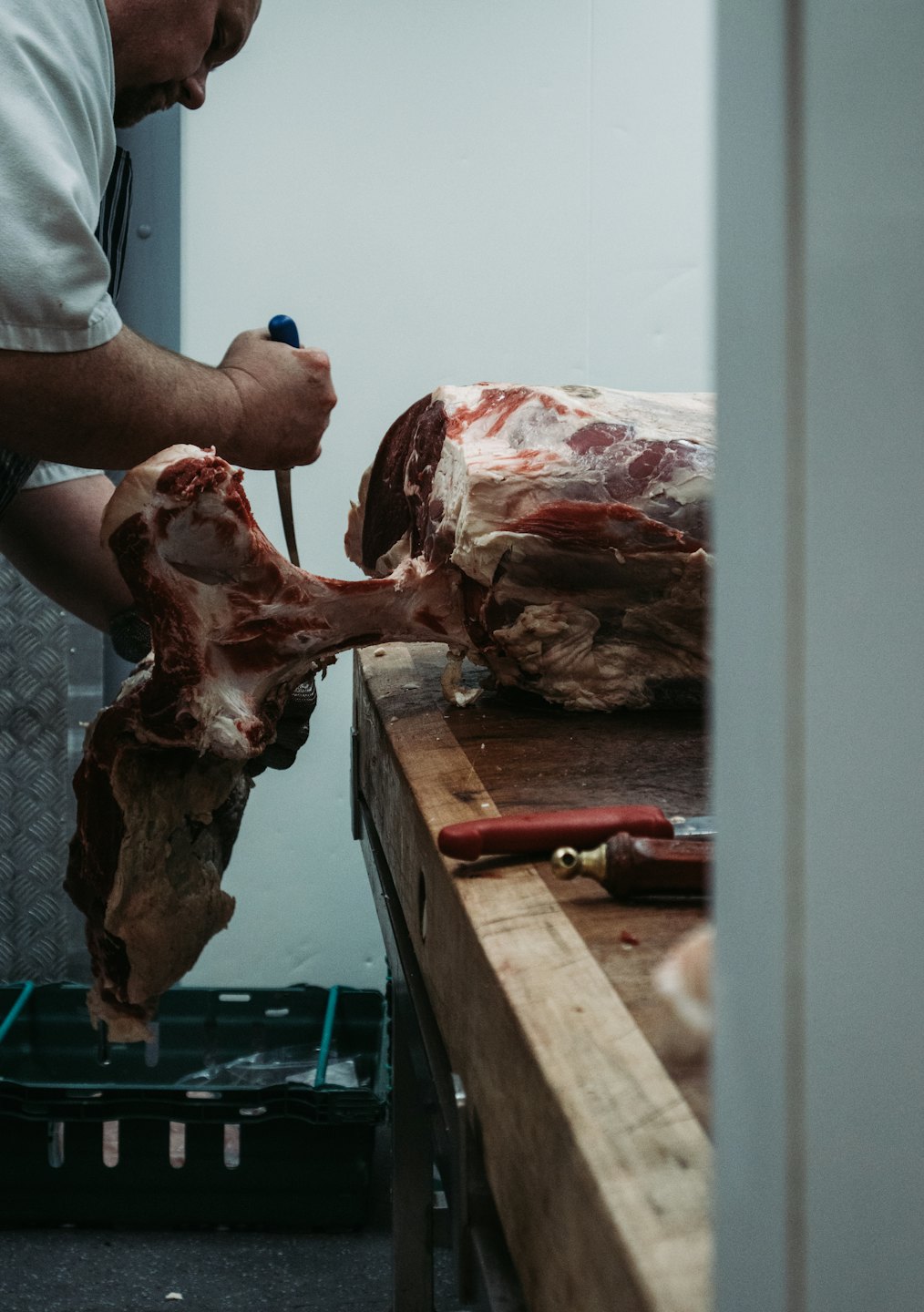 Butcher cutting a large piece of beef with bone on a wooden block.